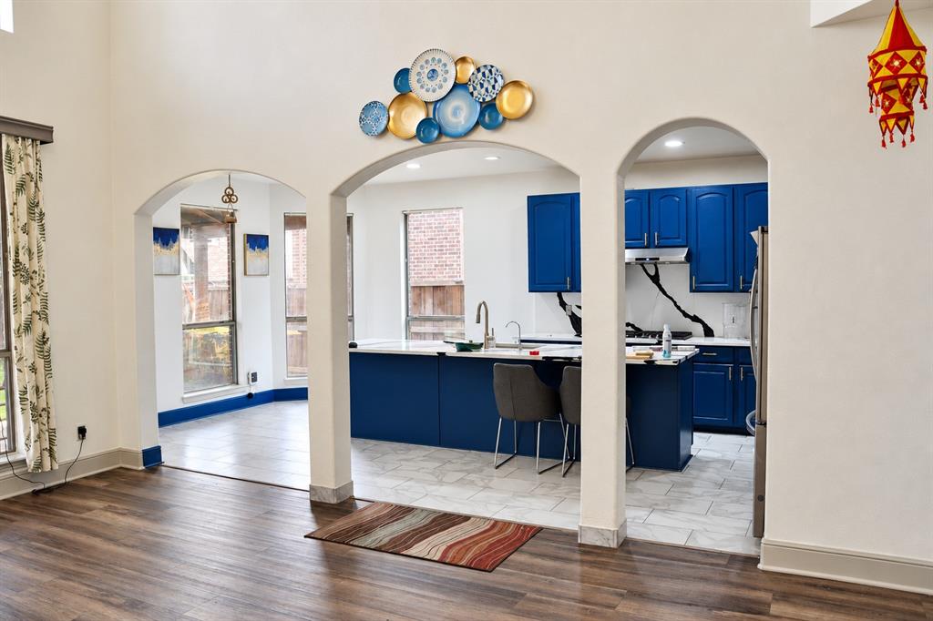 High-ceiling interior featuring arched architectural openings, kitchen island with built-in sink, vibrant cabinetry, and stone-finish flooring