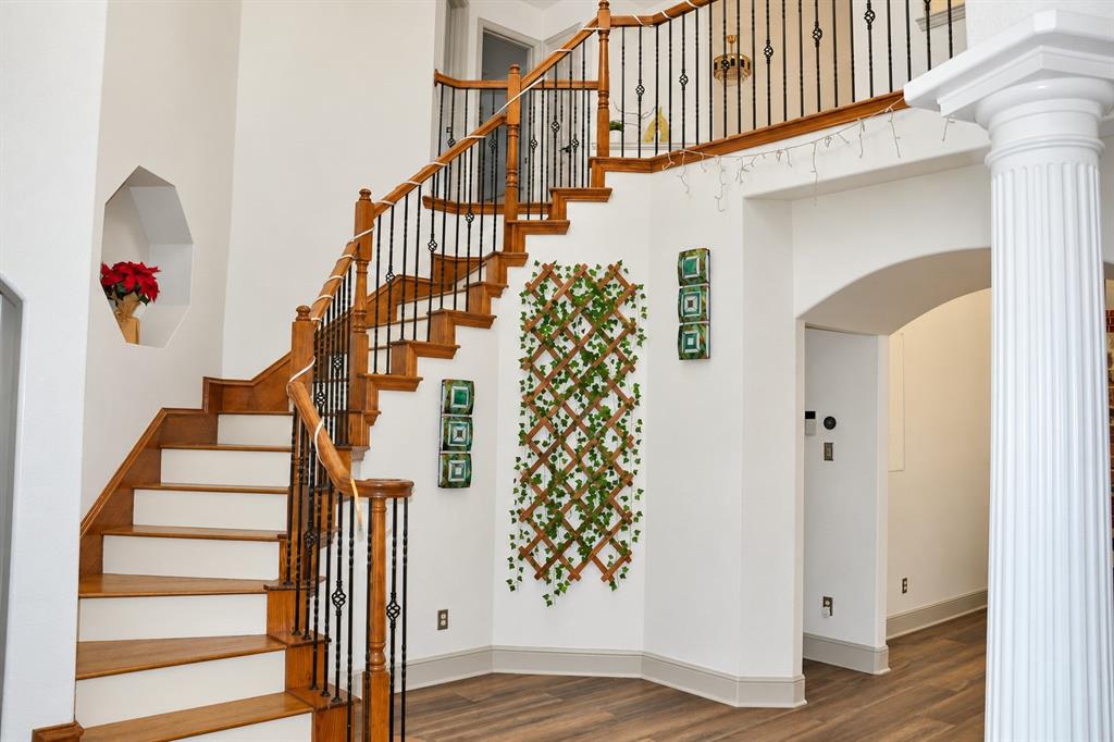Foyer featuring wood-finish flooring, a sweeping staircase with wooden handrails and iron balusters, a decorative wall niche, and a fluted structural column
