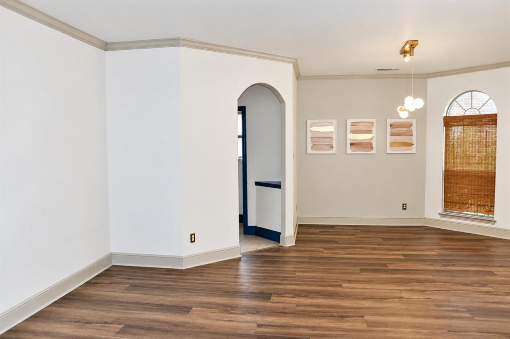 Interior space featuring wood-finish flooring, an arched entryway, crown molding, and a multi-globe pendant light fixture, complemented by an arched window
