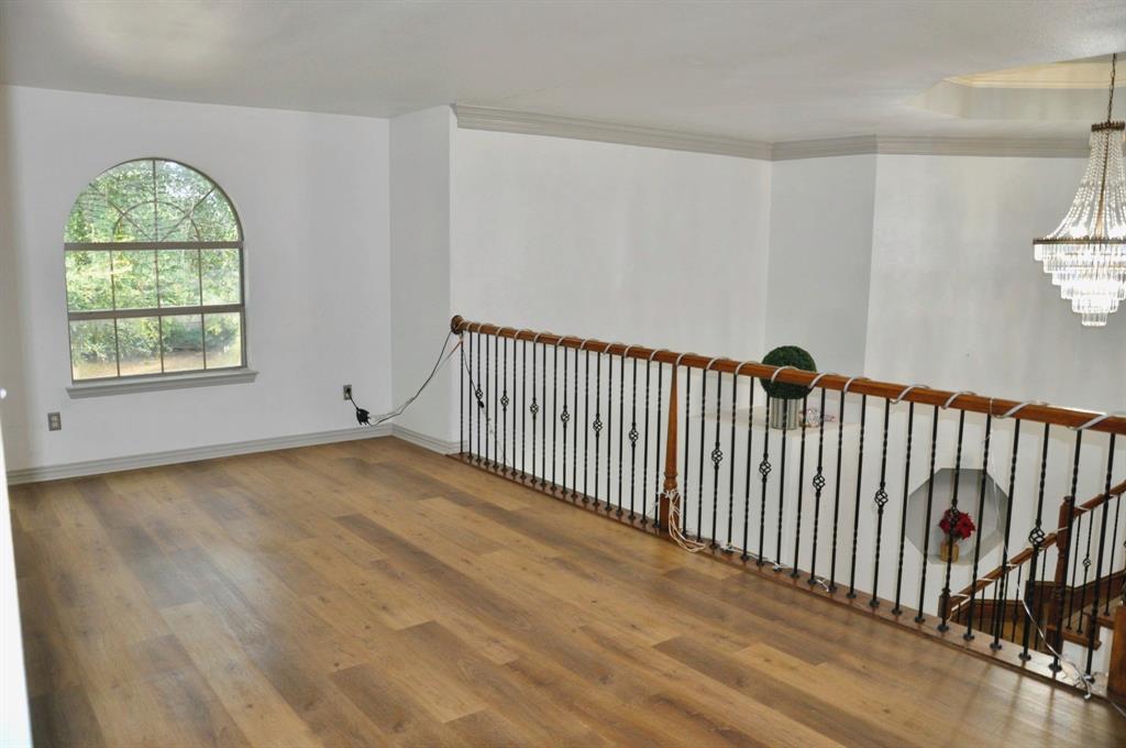 Open space featuring arched window, wood-finish flooring, metal baluster railing with wood handrail, and crystal chandelier