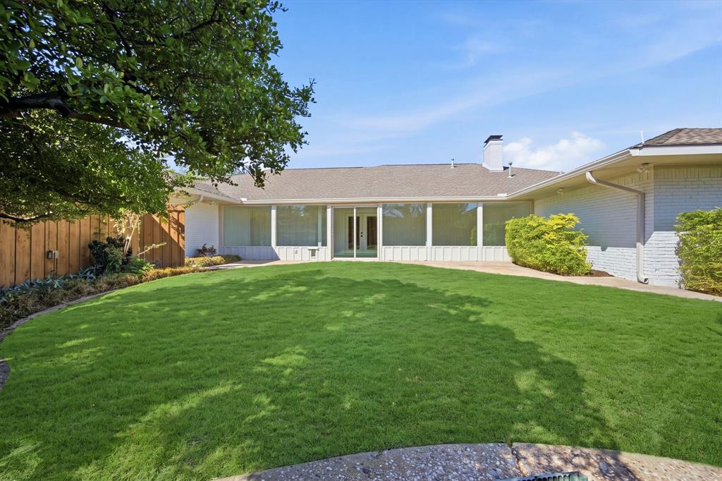 Expansive backyard featuring a manicured lawn, white brick exterior, floor-to-ceiling windows, a stone patio, and a wood privacy fence