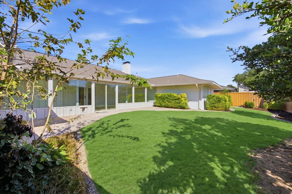Expansive backyard featuring a curved lawn, paved patio, mature landscaping, and an exterior brick chimney