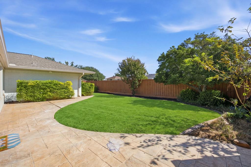 Backyard featuring a stamped concrete patio, manicured lawn, perimeter wood fencing, and established trees