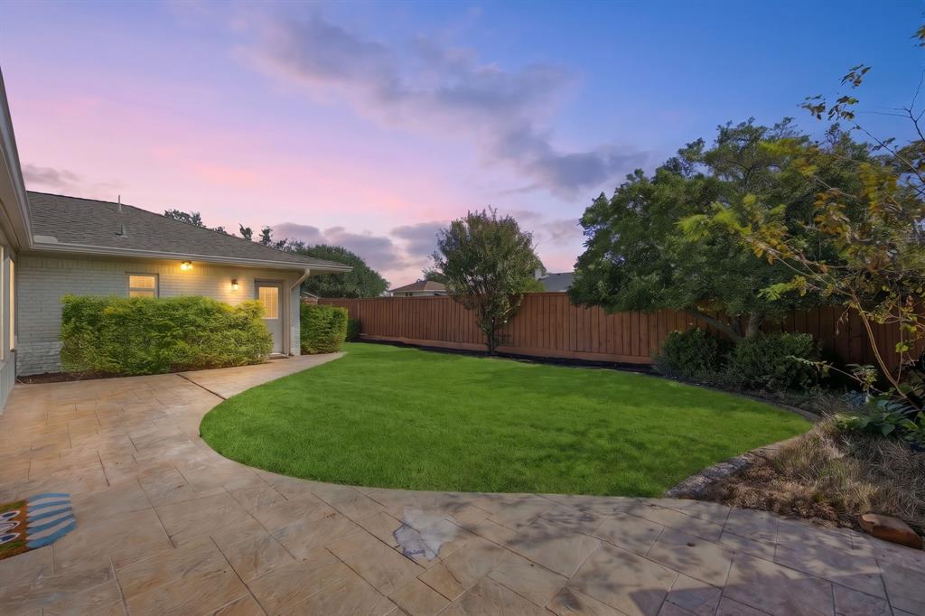 Rear exterior space featuring a stamped concrete patio, a manicured lawn, and a perimeter wood privacy fence