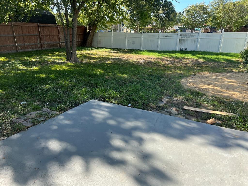 Backyard featuring a concrete patio, grass lawn, mature trees, and privacy fencing