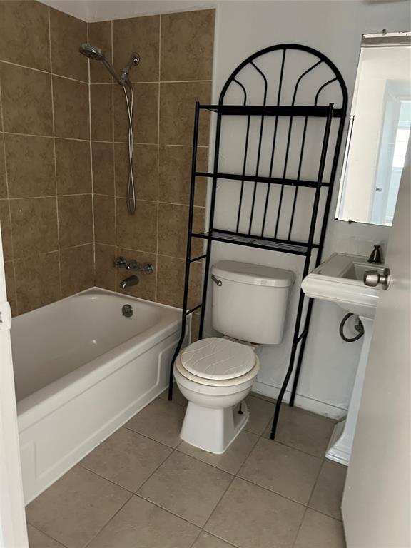 Bathroom featuring a porcelain-finish bathtub, wall-mounted shower head, tiled tub surround, pedestal sink, and floor tiling