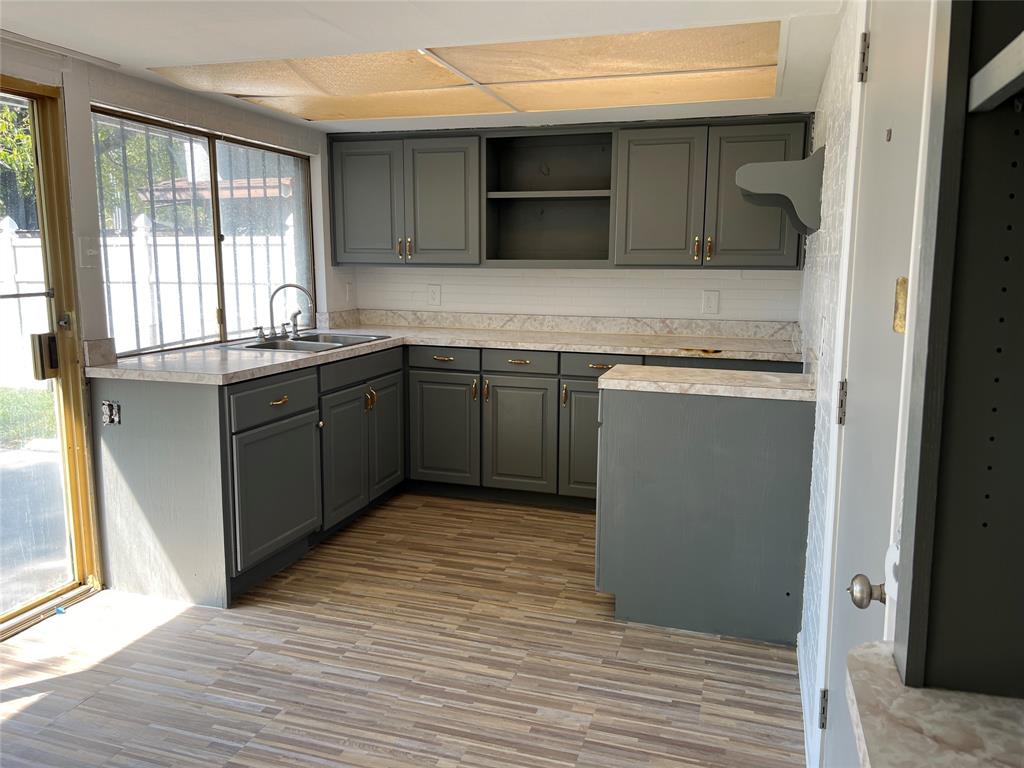 Kitchen featuring charcoal-toned cabinetry, stone-finish countertops, wood-finish flooring, dual-basin stainless steel sink, and a glass sliding door