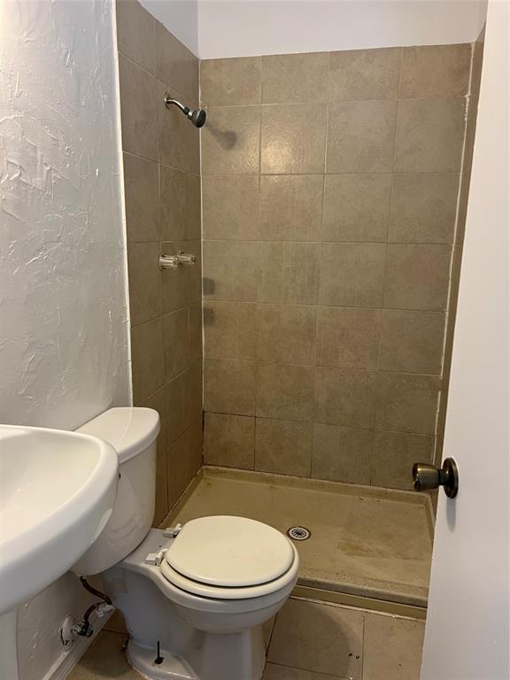 Shower stall featuring full-height square ceramic tile surround, integrated shower head, and floor-mounted toilet