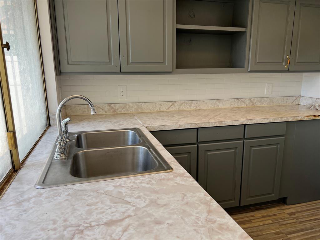 Kitchen featuring gray cabinetry, stone-patterned laminate countertops, white subway tile backsplash, stainless steel double-basin sink, and high-arc faucet