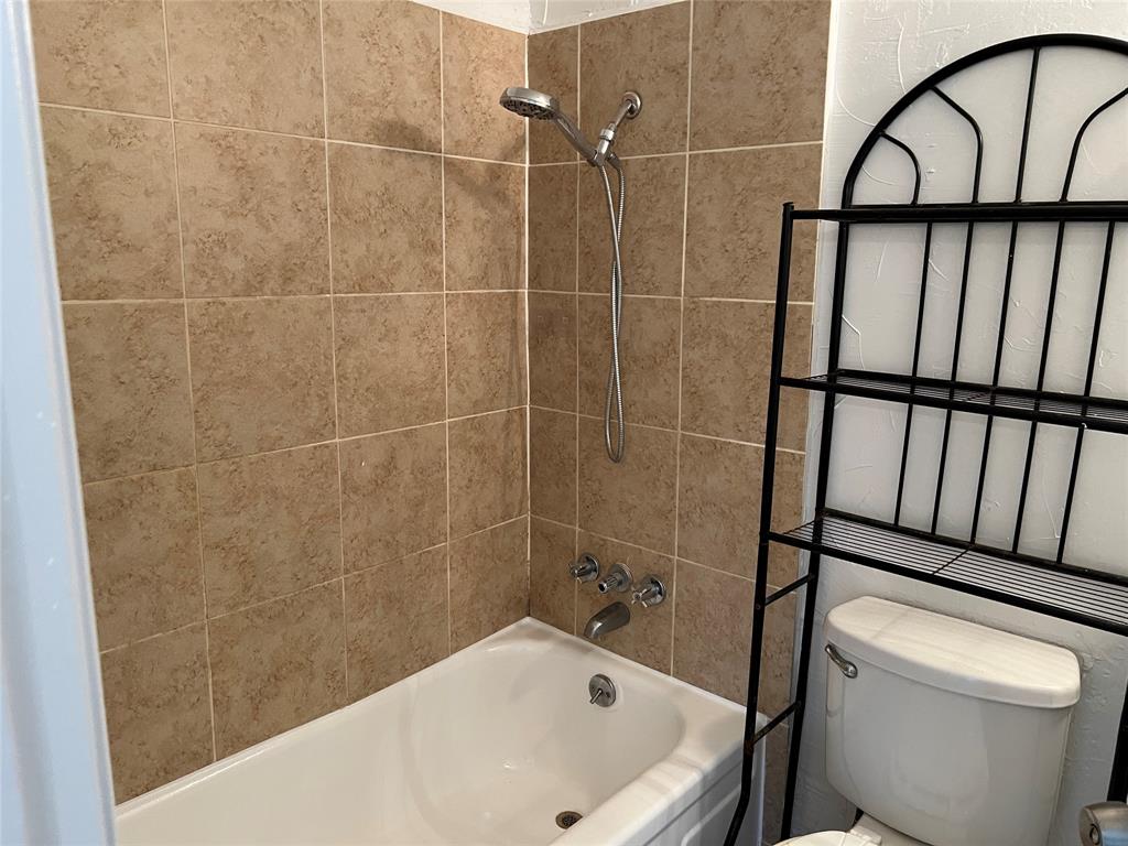 Bathtub with porcelain surround, beige ceramic wall tiling, and adjustable handheld shower head with chrome fixtures