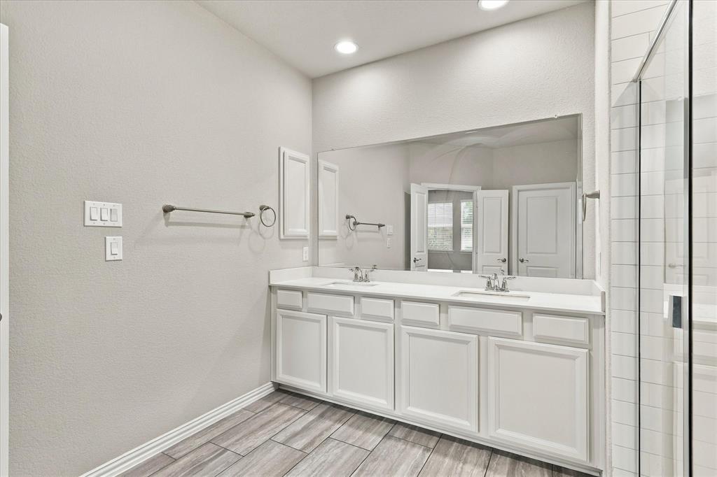 Dual-vanity cabinetry with white finish, solid surface countertop, expansive wall-mounted mirror, recessed lighting, and wood-finish flooring