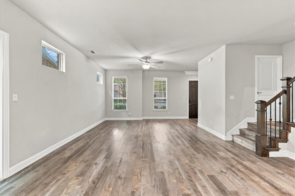 Open-concept interior featuring wood-finish flooring, multi-pane windows, ceiling fan, and a staircase with dark wood handrails and metal balusters