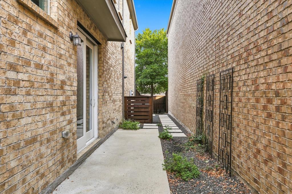 Side exterior featuring a brick facade, concrete walkway, gravel landscaping, metal wall trellises, and wood-slat privacy fencing