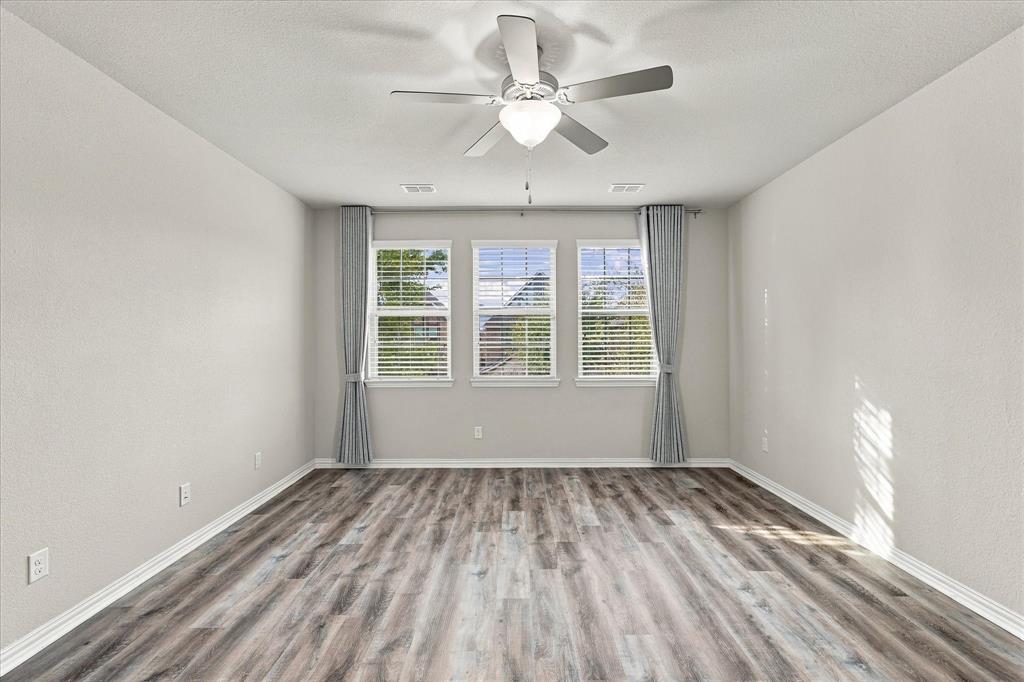 Room featuring wood-finish flooring, three windows with horizontal blinds, and a central ceiling fan with an integrated light fixture