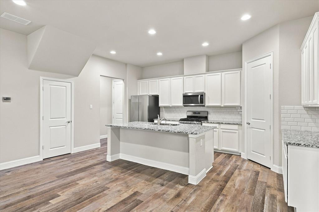 Kitchen featuring a central island with stone-finish countertops, white shaker-style cabinetry, subway tile backsplash, stainless steel appliances, and wood-finish flooring