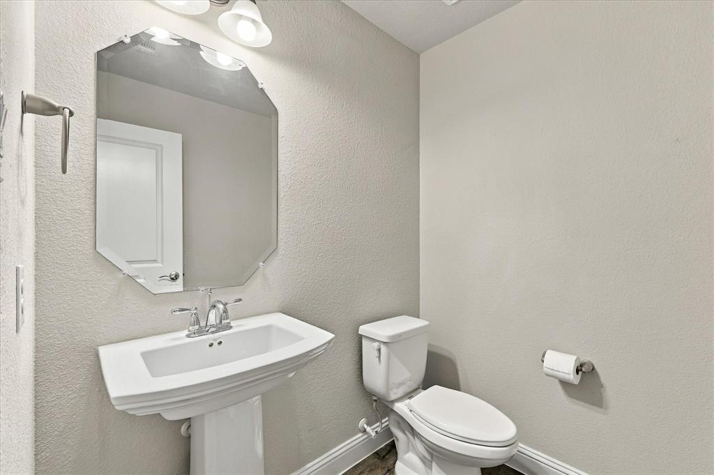 Powder room featuring a white pedestal sink, chrome dual-handle faucet, octagonal wall-mounted mirror, and brushed-finish metal towel bar