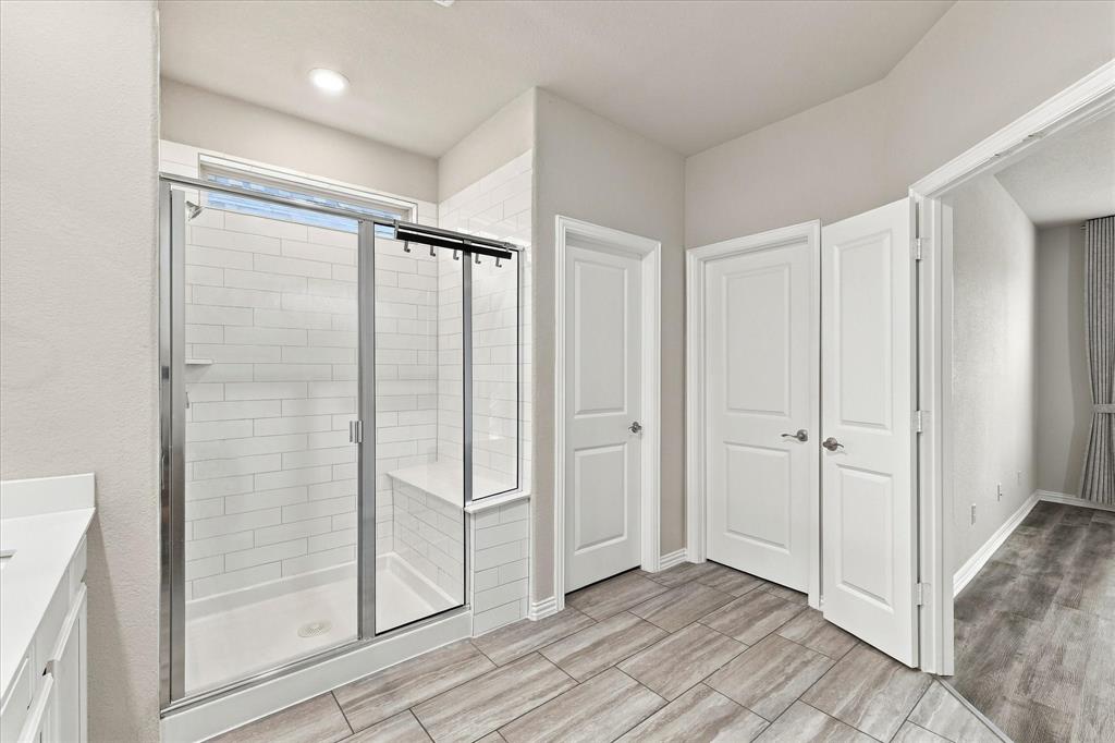 Walk-in shower featuring a built-in tiled bench, white subway tile surround, and chrome-framed glass enclosure, complemented by wood-finish floor tiling