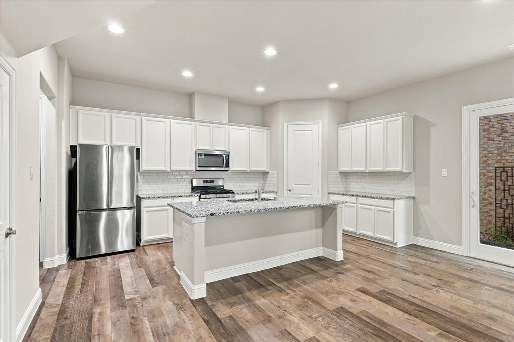 Kitchen featuring white shaker-style cabinetry, stone-finish countertops, subway tile backsplash, stainless steel appliances, and wood-finish flooring