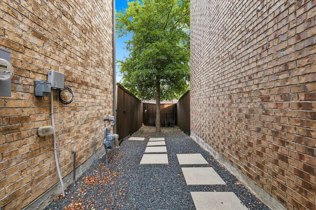 Side yard featuring tan brick exterior walls, stone paver pathway, gravel ground cover, and enclosed wood fencing