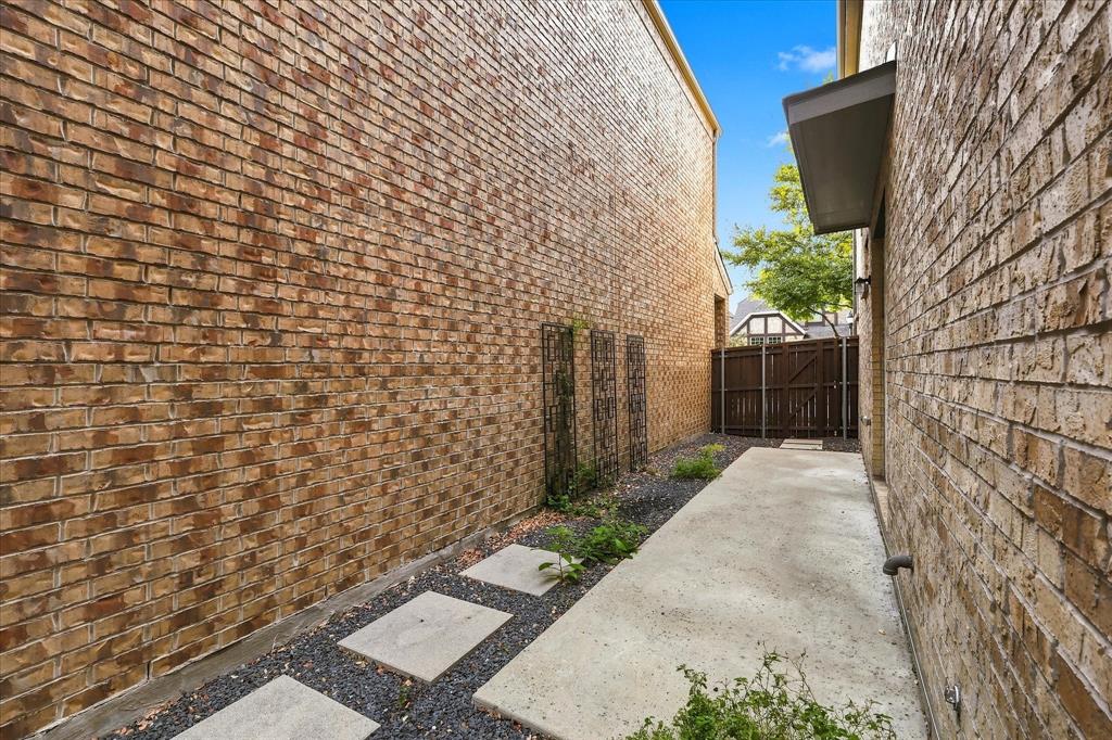 Exterior side yard featuring full brick siding, concrete paver pathway, decorative metal wall trellises, and a wood privacy fence