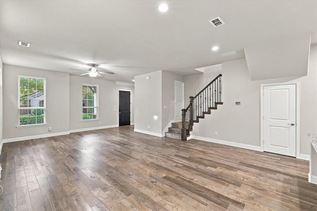 Open-concept interior featuring wood-finish flooring, recessed lighting, and a staircase with a dark-stained wood handrail and iron balusters