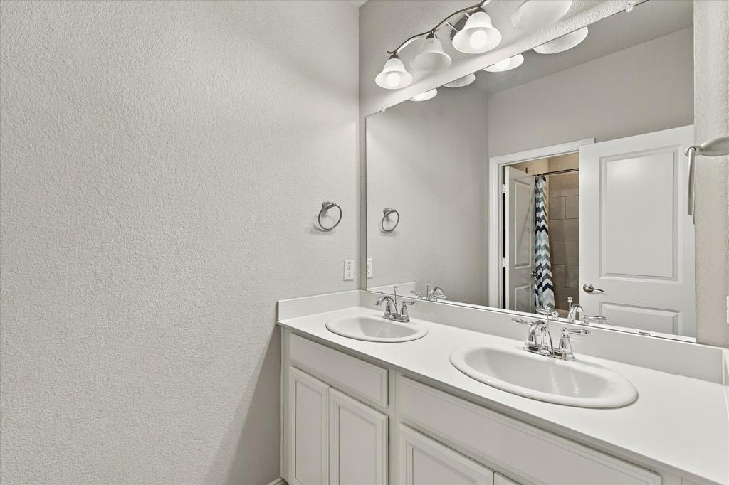 Double vanity with white cabinetry, solid-surface countertop, dual drop-in sinks, polished chrome fixtures, and a wall-to-wall mirror