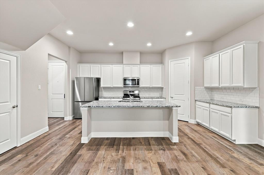 Kitchen featuring white cabinetry, stone countertops, stainless steel appliances, a central island with an integrated sink, and wood-finish flooring