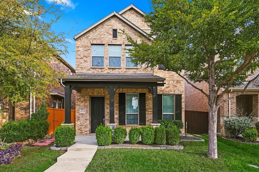 Multi-story brick exterior featuring a covered front porch, dark-toned architectural columns, black shutters, and manicured landscaping