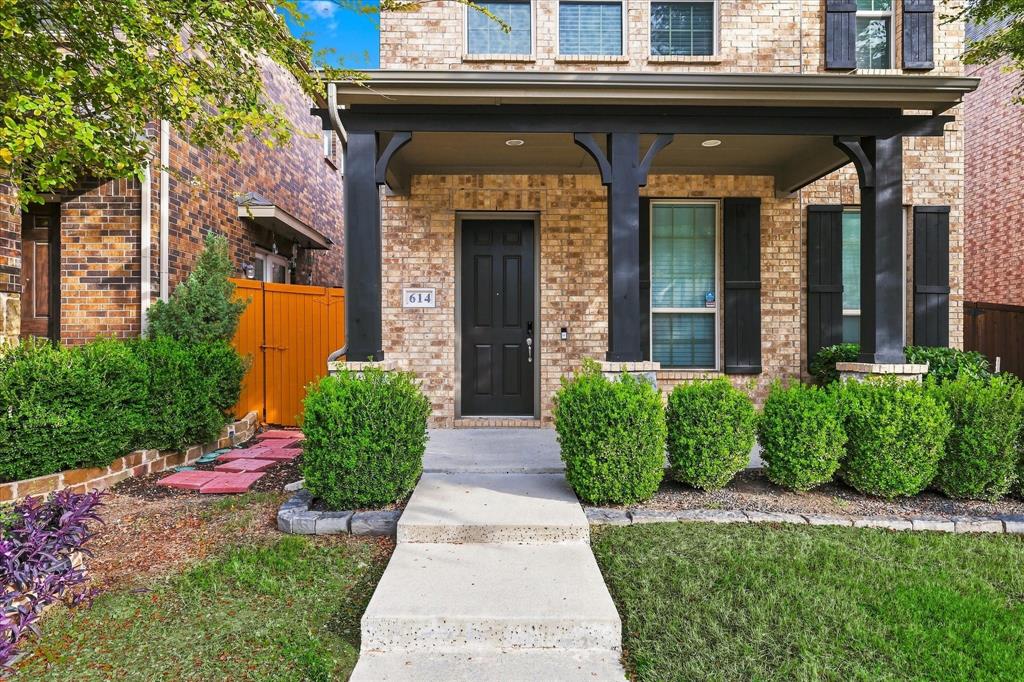 Brick exterior featuring a covered front porch, dark-toned support columns, shutters, and a manicured landscape