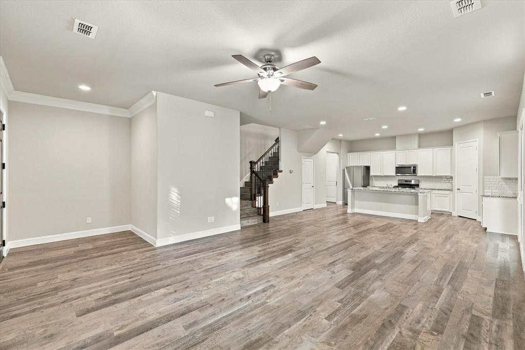 Open-concept interior featuring wood-finish flooring, recessed lighting, a ceiling fan, white cabinetry with stone countertops, and a staircase with stained wood railings