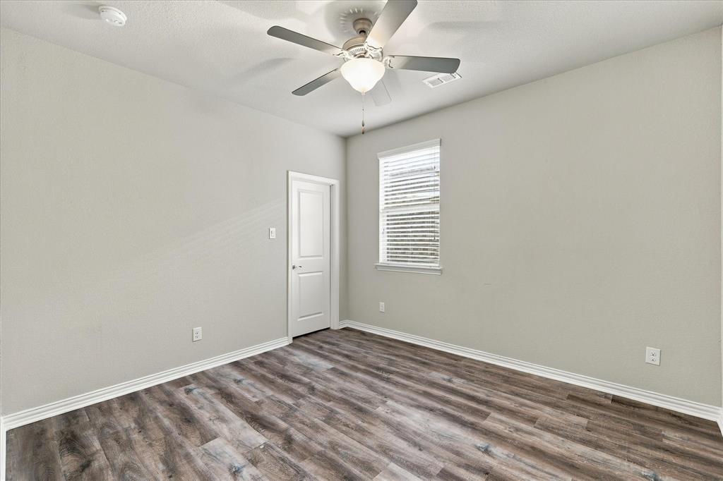 Room featuring wood-finish flooring, a ceiling fan with integrated lighting, and a window with blinds