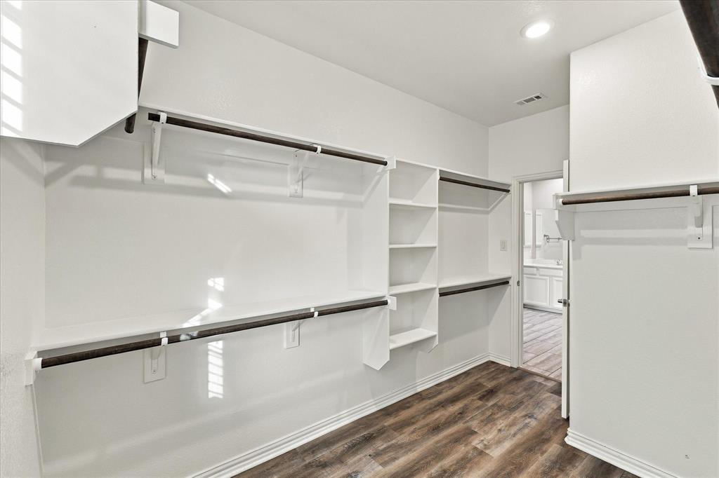 Walk-in storage area featuring custom white built-in shelving, dark metal hanging rods, and wood-finish flooring with integrated recessed lighting