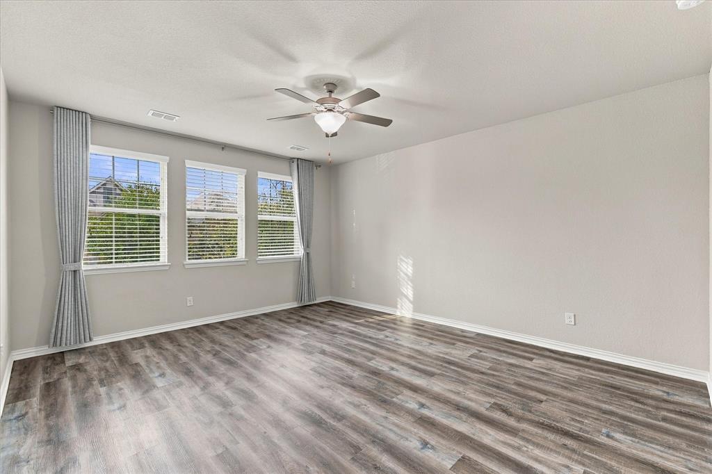 Room featuring wood-finish flooring, three windows with horizontal blinds, and a multi-blade ceiling fan