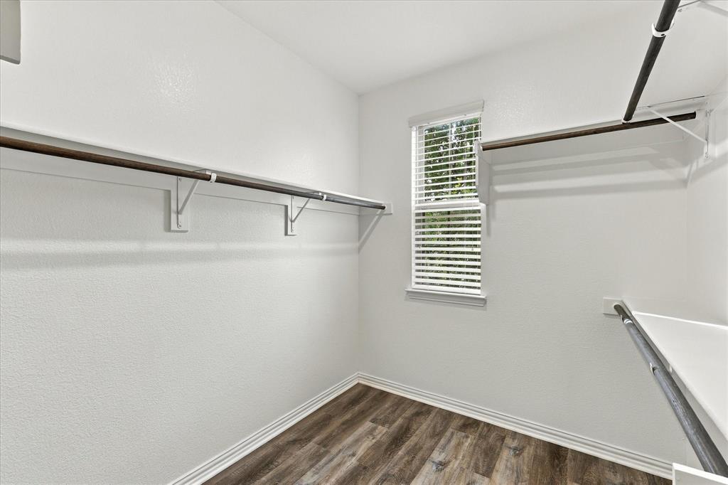 Walk-in closet featuring wood-finish flooring, white walls, horizontal window blinds, and tiered metal shelving rods