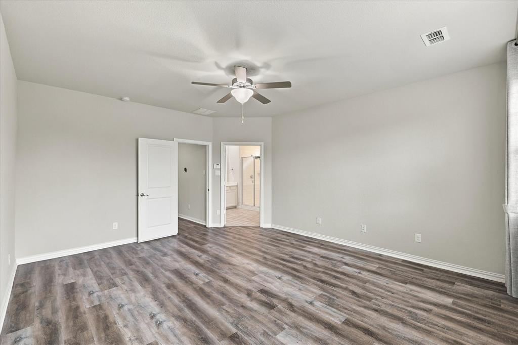 Neutral-toned room featuring wood-finish flooring, a multi-blade ceiling fan with integrated lighting, and solid-core interior doors