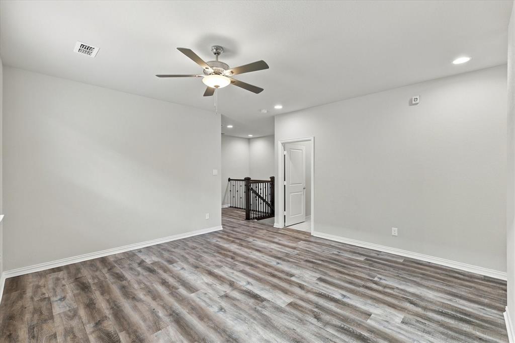 Interior room featuring wood-finish flooring, a multi-blade ceiling fan with integrated lighting, recessed ceiling lights, and iron stair railing
