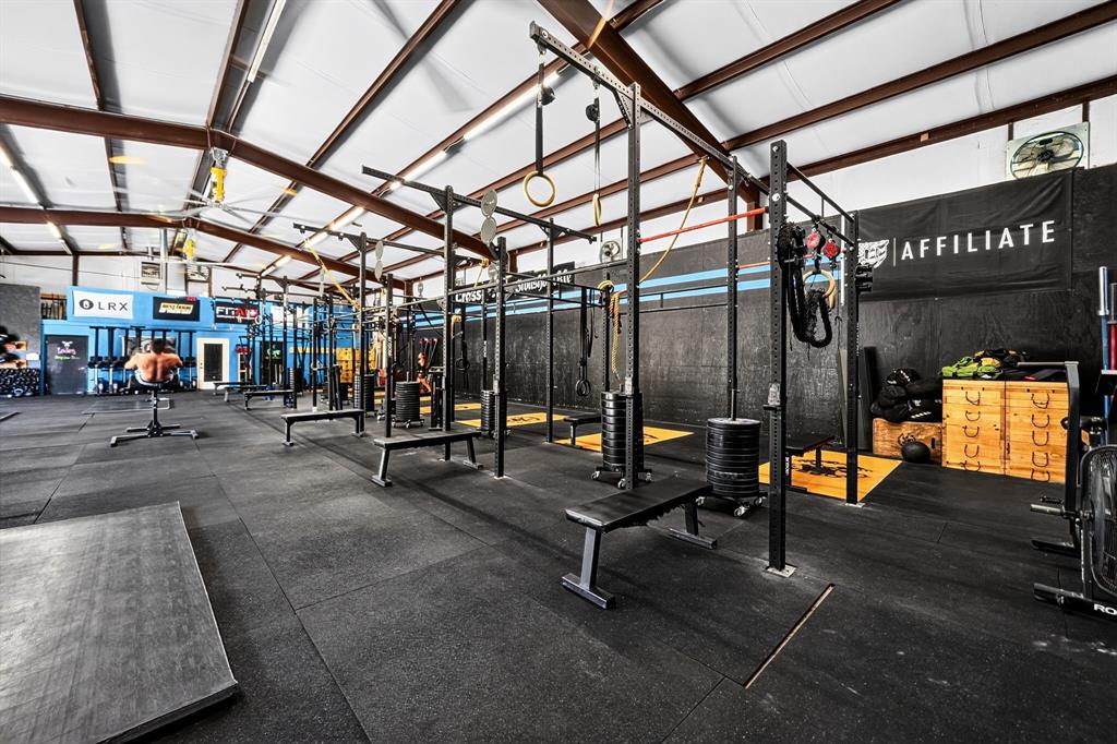 Open-concept fitness space featuring high-clearance vaulted ceilings with exposed steel beams, industrial lighting, durable rubberized flooring, and an expansive multi-station steel structural racking system