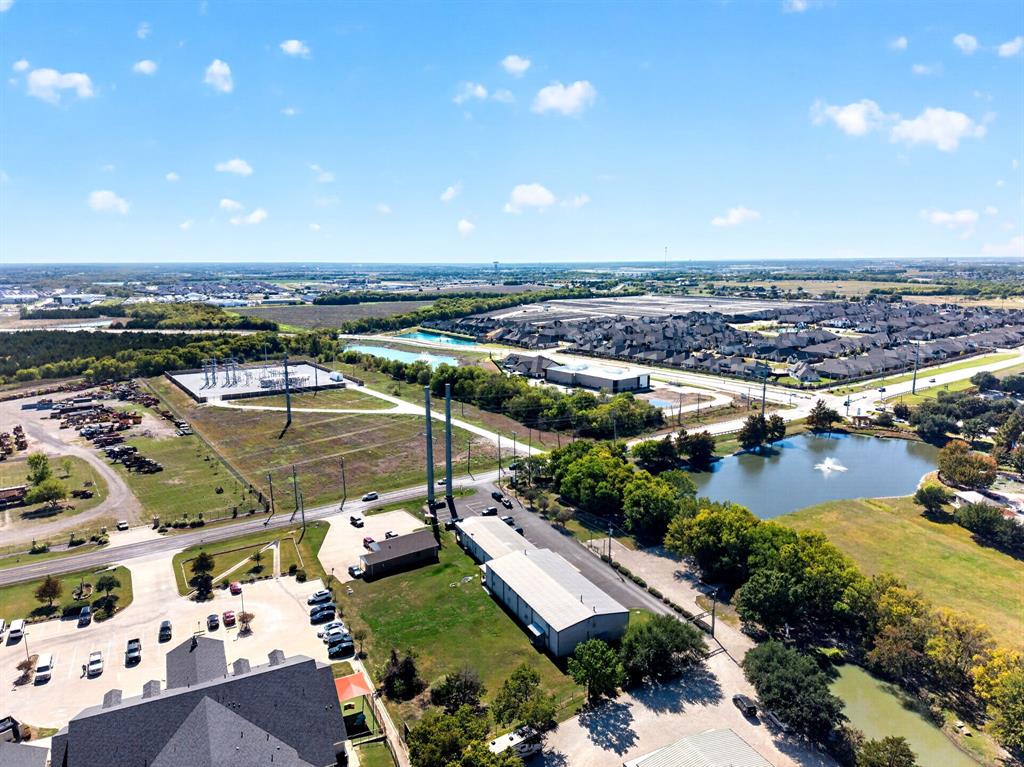 Aerial perspective showcasing expansive acreage, a scenic pond with a fountain, mature tree clusters, and direct access to paved thoroughfares