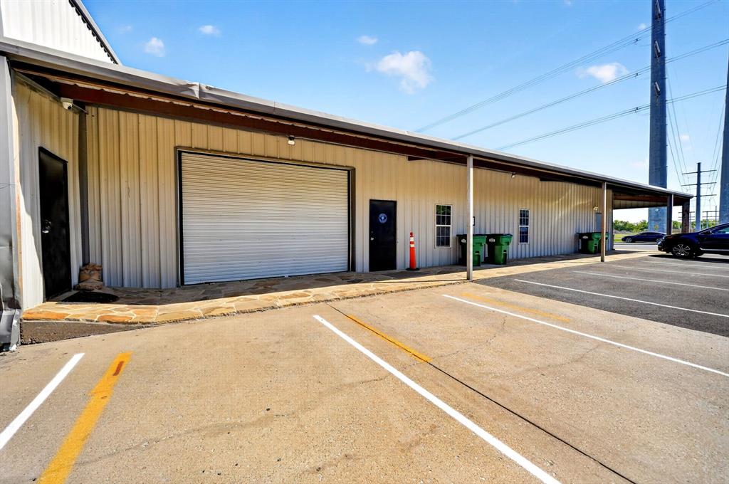 Metal-sided commercial exterior featuring a roll-up garage door, stone walkway, multiple access doors, and dedicated asphalt parking