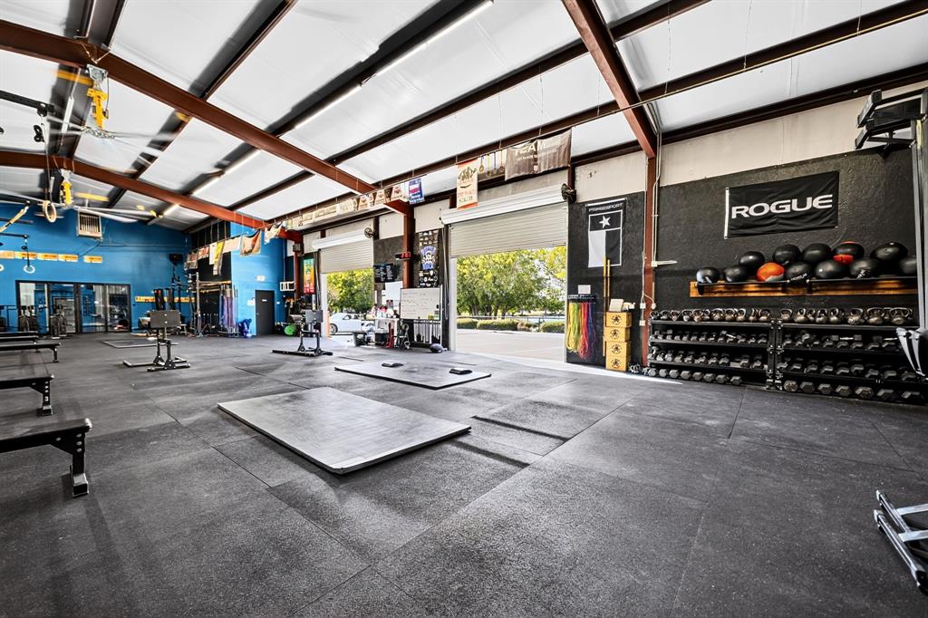 Expansive open-concept utility space featuring exposed steel beam framing, high-clearance vaulted ceilings, industrial roller-style bay doors, and durable rubberized flooring