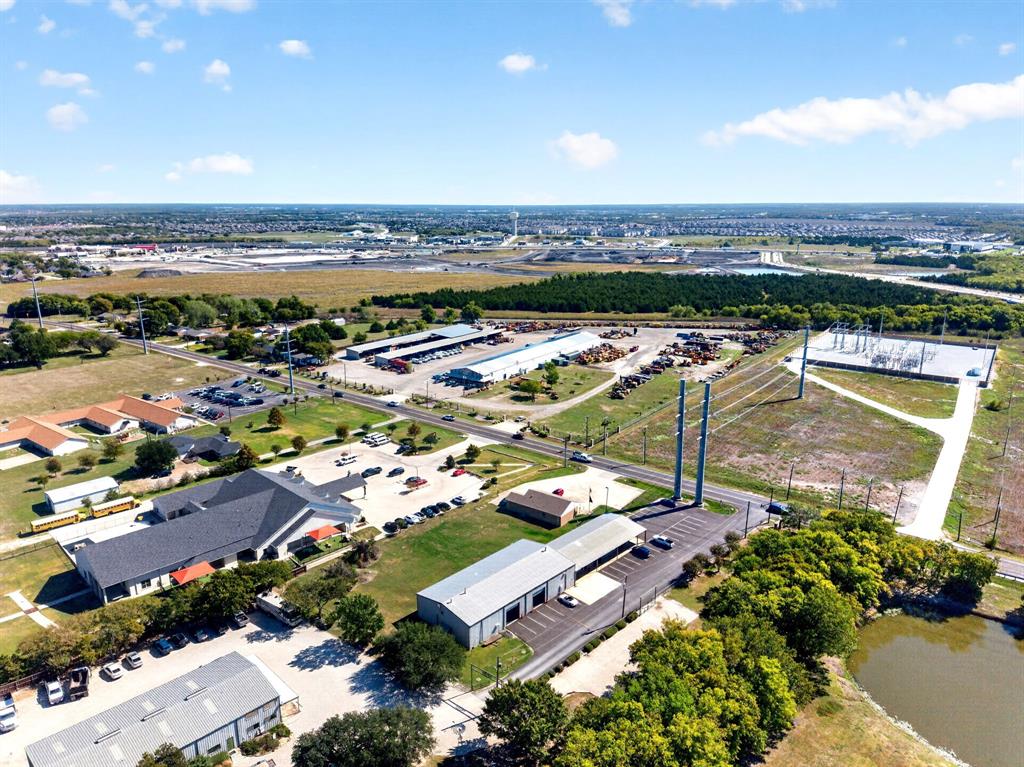 Aerial perspective of a multi-structure commercial property featuring expansive asphalt parking areas, covered storage bays, metal-roofed industrial buildings, and direct access to paved roadways