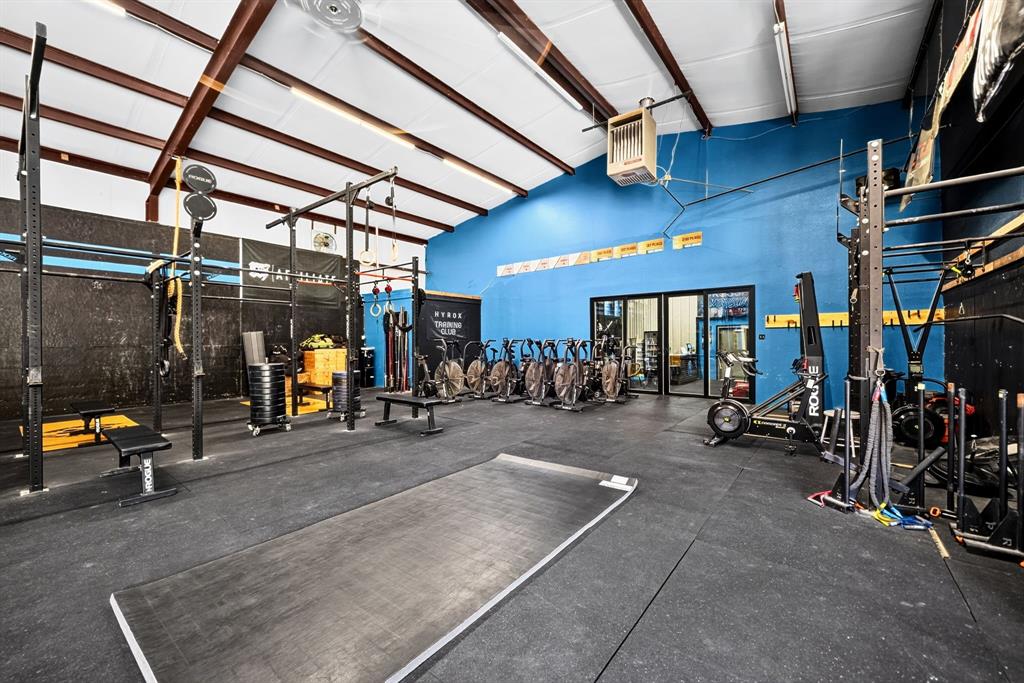 High-ceiling recreational space featuring exposed structural steel, rubberized flooring, integrated wall-mounted heater, and glass-paneled entry doors