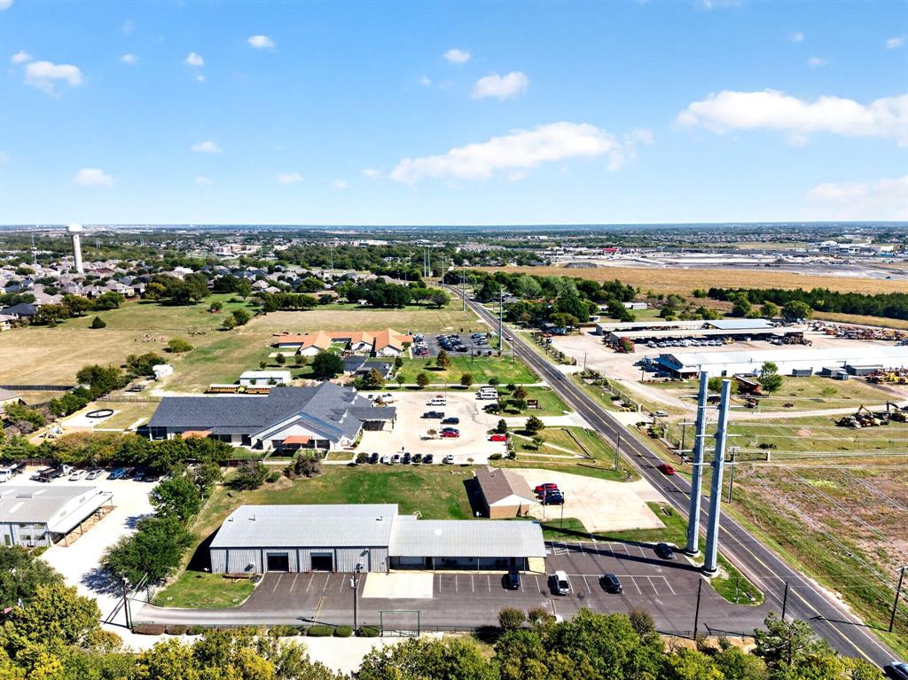 Aerial perspective of the property featuring a metal-sided commercial warehouse, an asphalt parking lot, two prominent steel support pillars, and direct frontage to a paved roadway