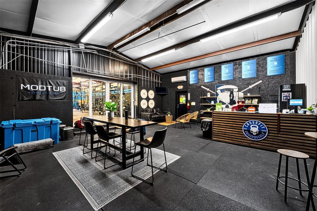 Industrial-style interior space featuring exposed metal ceiling beams, recessed linear lighting, rubberized flooring, and a built-in horizontal slat-front service counter