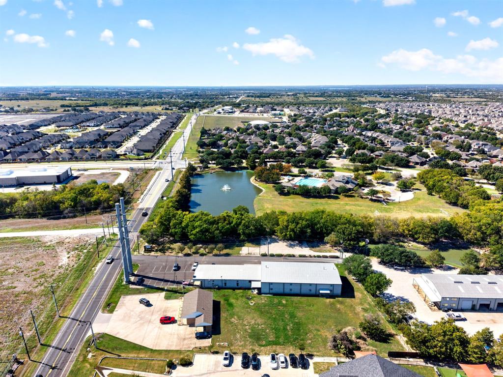 Aerial perspective of property featuring paved surface parking, metal-roof structure, and expansive open green space