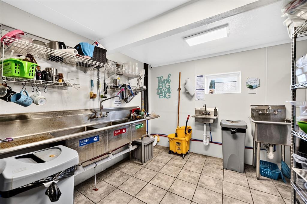 Utility area featuring a multi-basin stainless steel commercial sink, a wall-mounted stainless steel utility basin, tile flooring, and integrated wire shelving