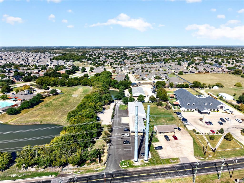 Aerial perspective of the property featuring asphalt parking areas, multiple structures, established landscaping, and bordering water features