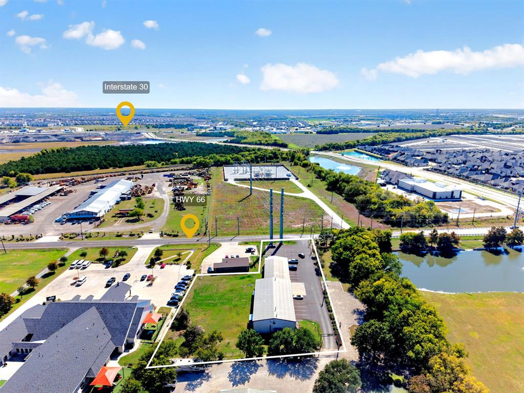 Aerial view of commercial property featuring a metal-sided building, paved parking surface, mature perimeter trees, and highway proximity