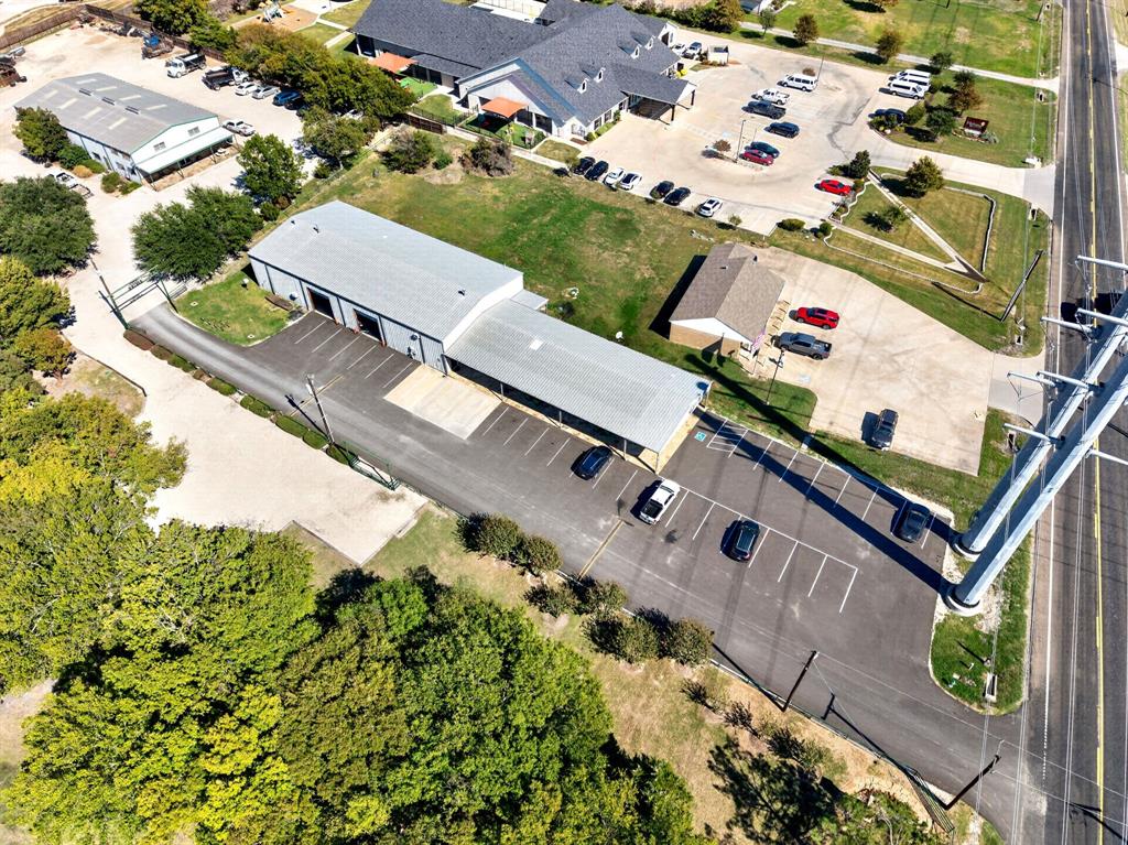 Commercial property featuring a metal-sided building, expansive paved parking lot, covered exterior loading area, direct road access, and mature perimeter trees