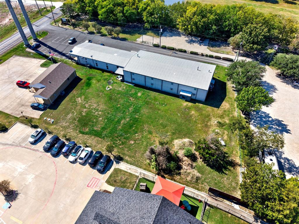 Aerial perspective featuring multiple industrial structures, expansive open green space, paved parking areas, and mature perimeter trees